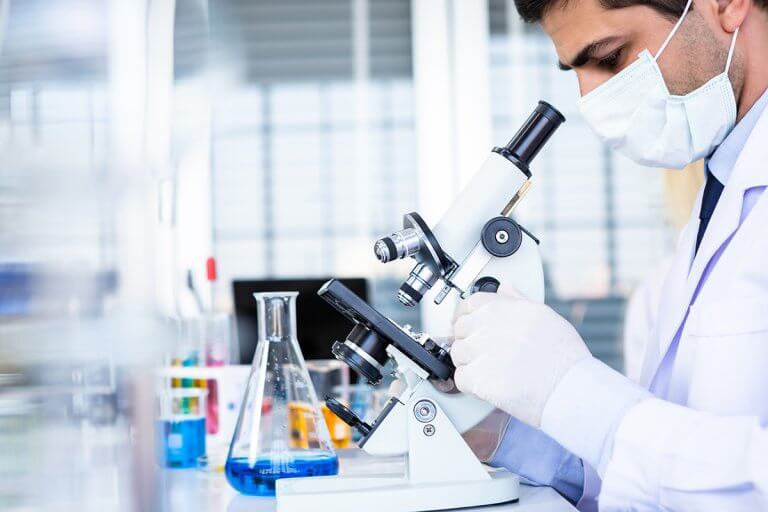 Male,Scientist,Working,Looking,At,Microscope,With,Sample,Test,Tube